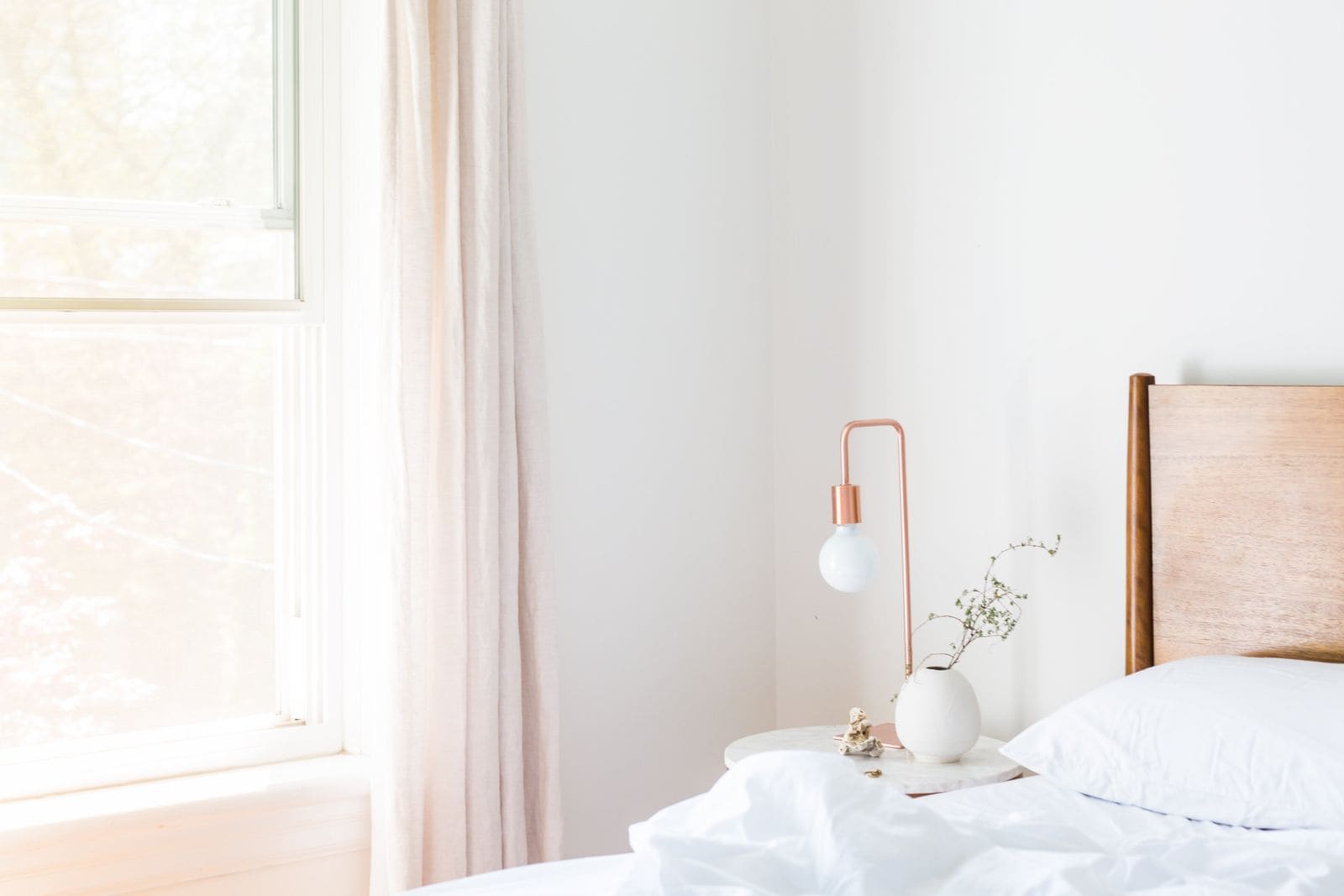 Bright minimalist bedroom with a white table lamp and vase on the nightstand