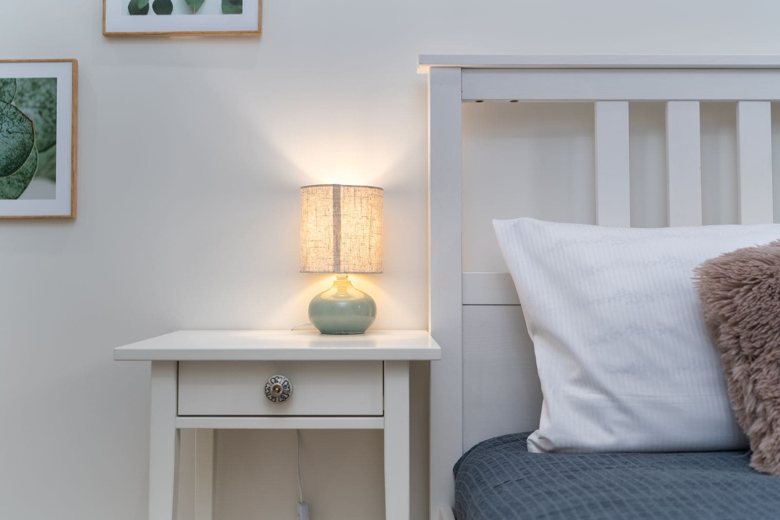 Cosy bedroom corner with a lit lamp on a white nightstand beside the bed