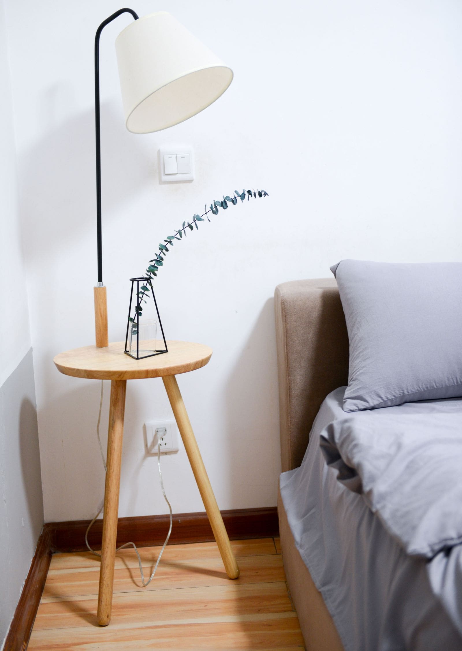 Modern bedroom with grey bedding, a wooden nightstand and a slim table lamp