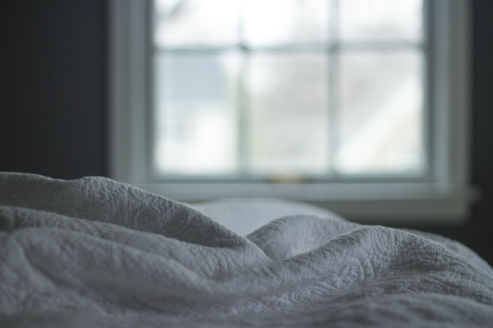 Quilted blanket on a bed beside a window in soft morning light