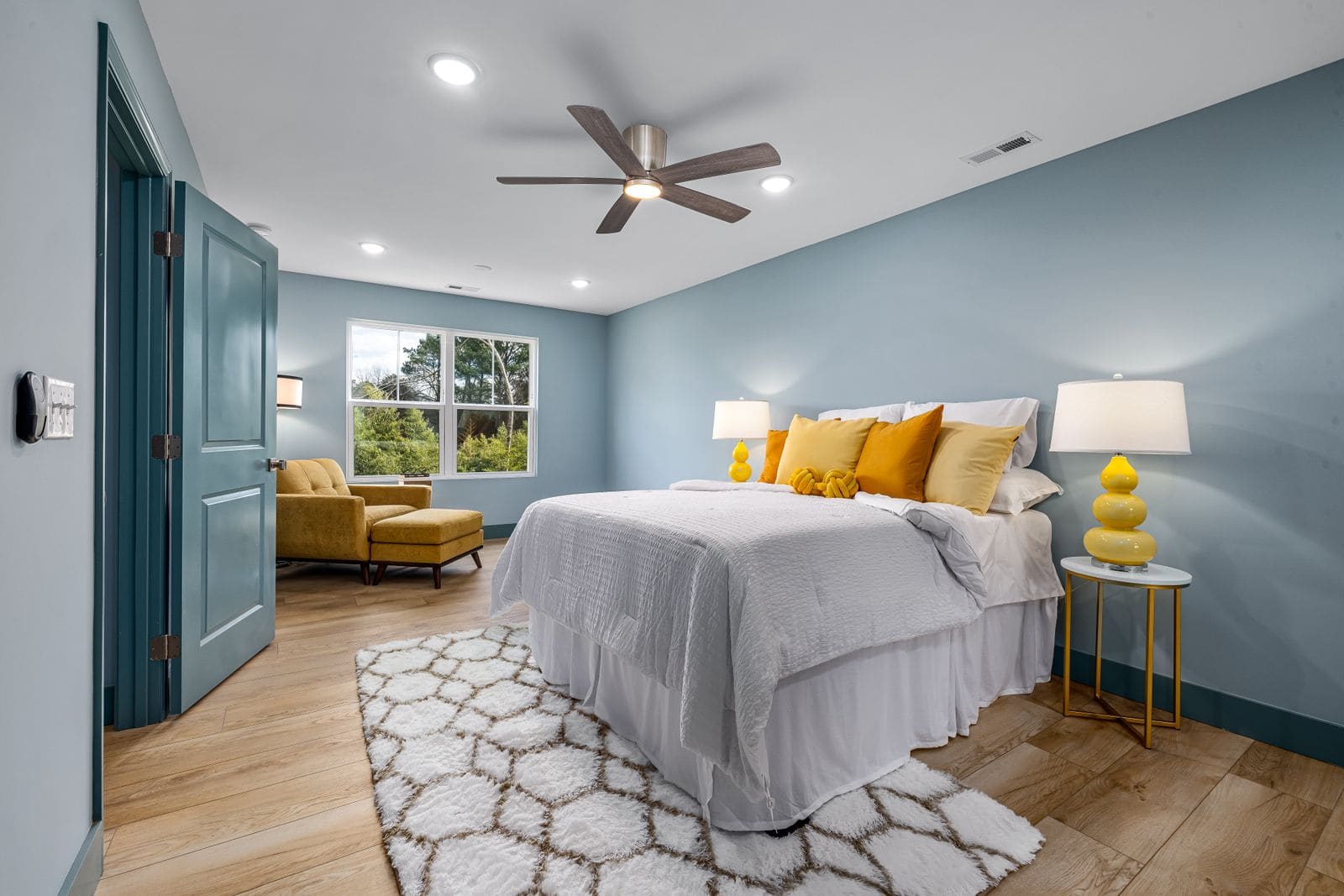 Bright bedroom with yellow accents, an armchair by the bed and a ceiling fan