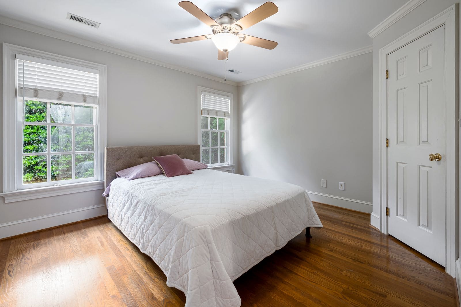 Bright bedroom with crisp white bedding, a ceiling fan and large windows